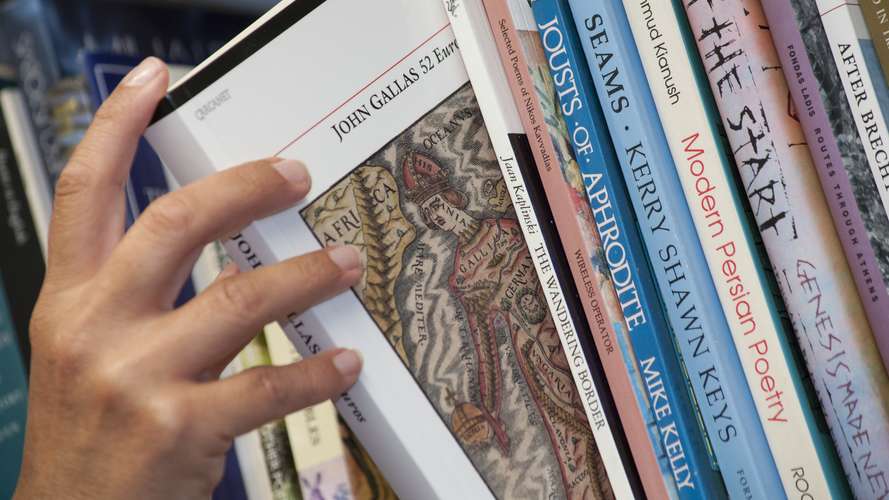 Hand retrieving John Gallas' 52 Euros from a bookshelf